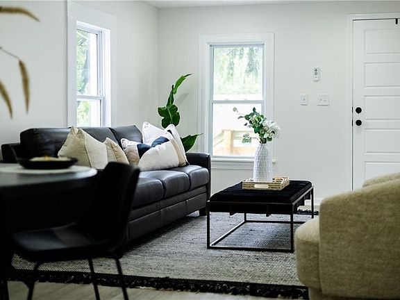 Bright interior space featuring light-toned walls, wood-finish flooring, a white paneled door with black hardware, and double-hung windows