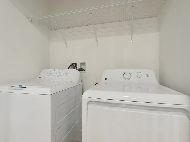 Modern laundry room with sleek white washer and dryer, complemented by practical overhead shelving.