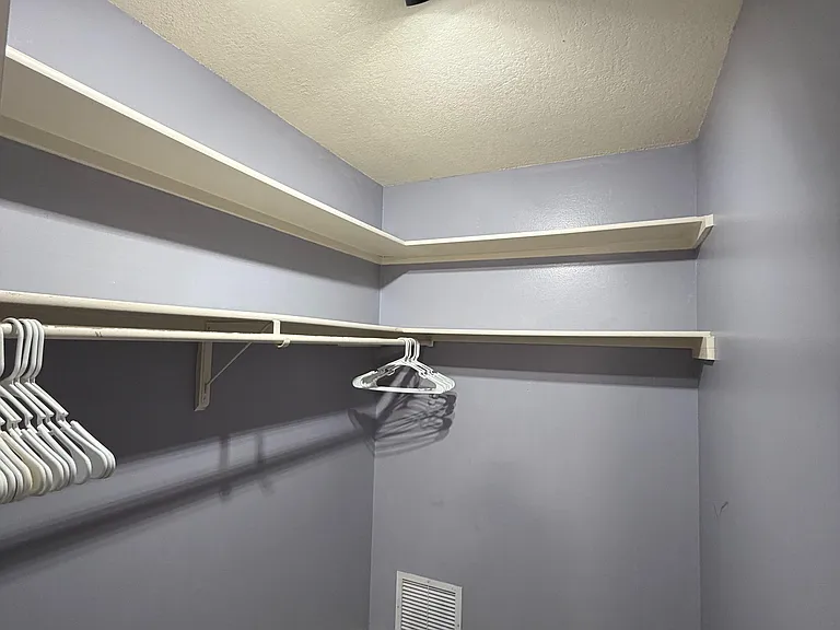 Spacious walk-in closet with double hanging rods, overhead shelving, and tiled flooring for easy upkeep.