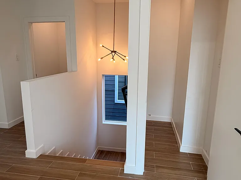 Open upstairs landing with wood-look tile flooring, tall ceilings, and a modern chandelier, connecting to nearby storage.