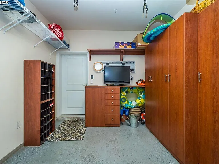 Inside of garage showing door to laundry room. Lots of storage cabinets and large workbench with tools. Overhead storage for bikes, stand up paddleboard, surfboard, beach chairs and floats, and beach paraphernalia.