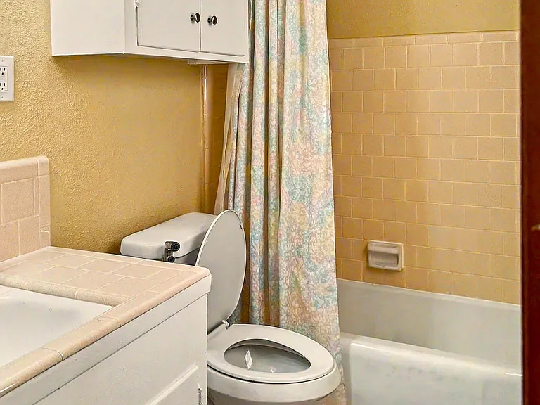 Full bathroom with tub/shower combo, tiled surround, and vanity storage plus an over-toilet cabinet for essentials.
