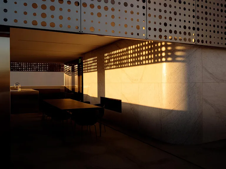 Outdoor Terrace Dining with Architectural Light Play _ As the sun sets, the perforated metal panels cast dynamic patterns of light and shadow across the terrace, enhancing the ambiance of this open-air dining space.
