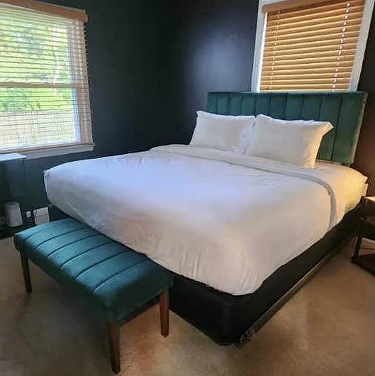 Bedroom features a full/queen bed with upholstered headboard, matching bench, and two windows with blinds for privacy.