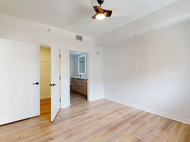 Spacious apartment bedroom with large closet, attached bathroom and wood style flooring.