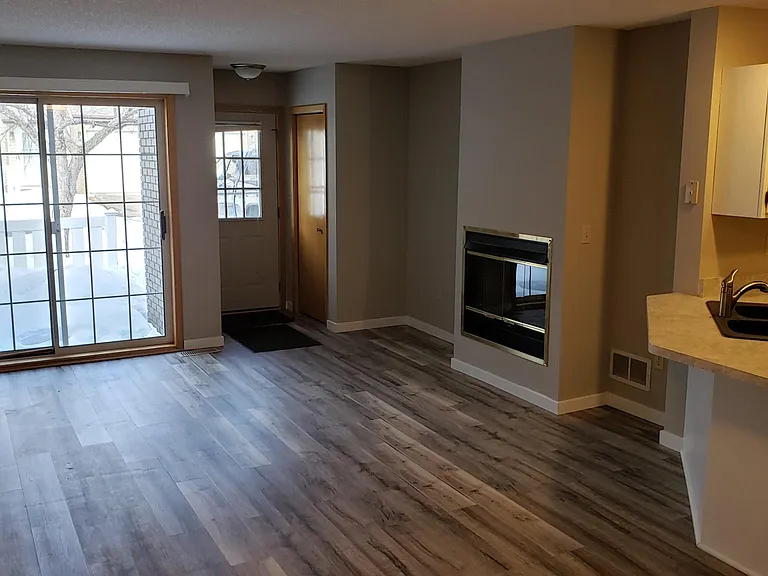 Large living room with gas fireplace, patio door with blinds. New Luxury Vinyl Tile floor grey tone floor and walls.