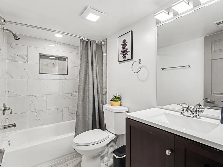 Updated full bath with tiled tub/shower surround, large vanity with mirror, and convenient built-in shower niche.