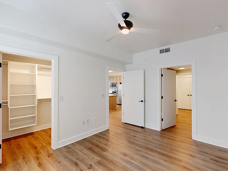 Spacious apartment bedroom with large closet, attached bathroom and wood-style flooring.