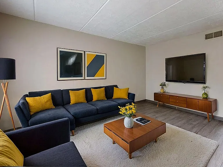 Contemporary living room with a sleek navy sofa accented by vibrant yellow pillows, featuring a stylish coffee table and a modern entertainment space.