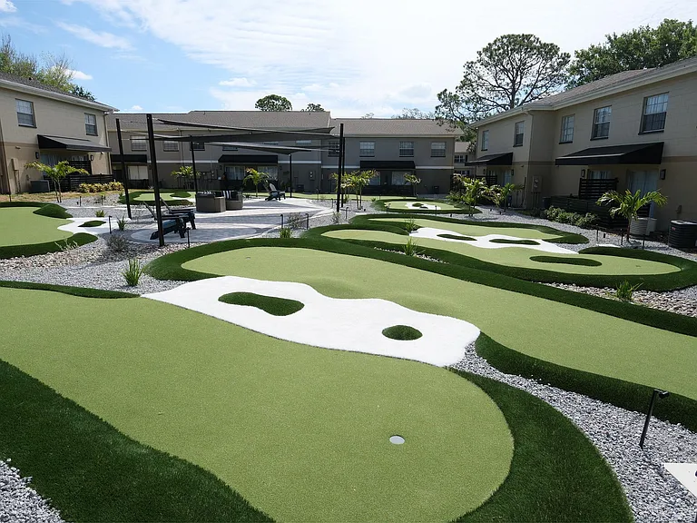 Luxurious apartment complex featuring an expertly designed mini-golf course surrounded by lush greenery and modern outdoor seating areas.