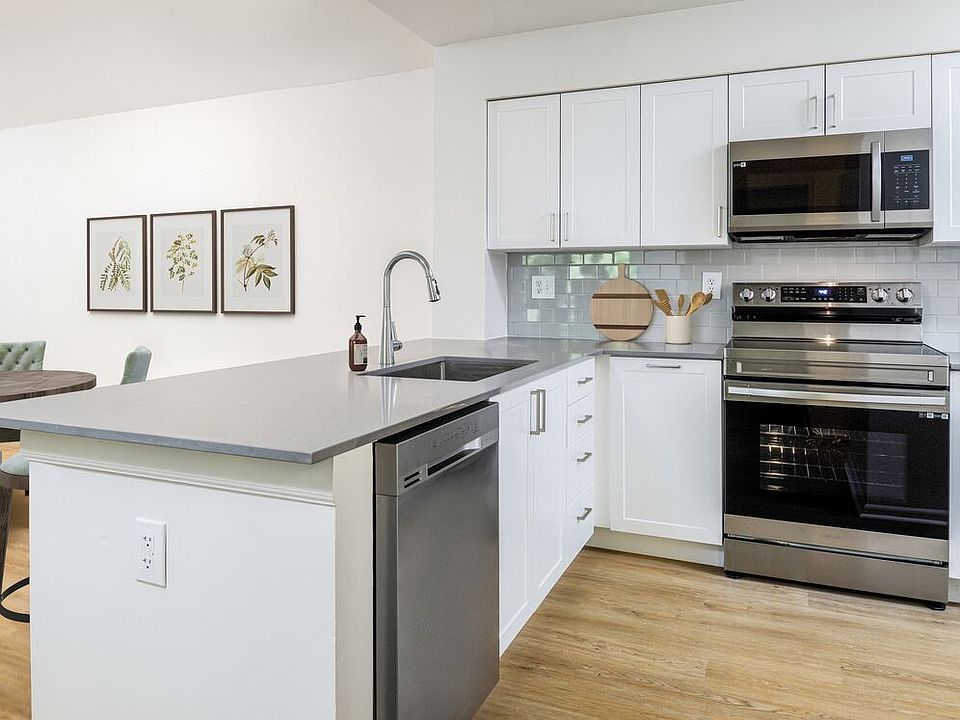 Renovated Package III kitchen with stainless steel appliances, grey quartz countertops (select homes), white cabinetry, light grey tile backsplash, and hard surface flooring