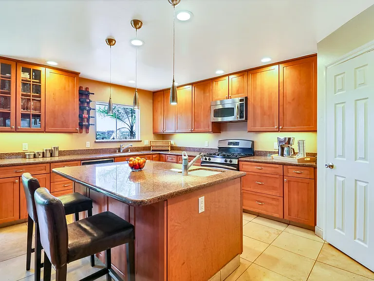 Large, bright kitchen with canyon view includes expansive granite countertops, custom cabinetry, and large cafe height kitchen island with bar sink. Door leads to large walk in pantry.