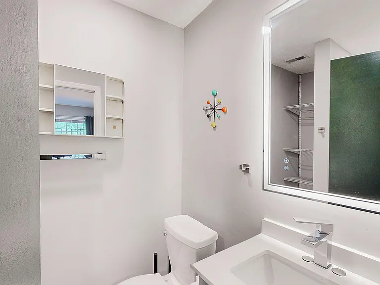 Clean bathroom with a wide vanity, modern faucet, large mirror, and built-in shelving plus nearby storage closet.