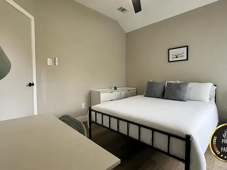 Private bedroom with a full bed, dresser storage, and a work desk, plus a ceiling fan and bedside table for daily comfort.