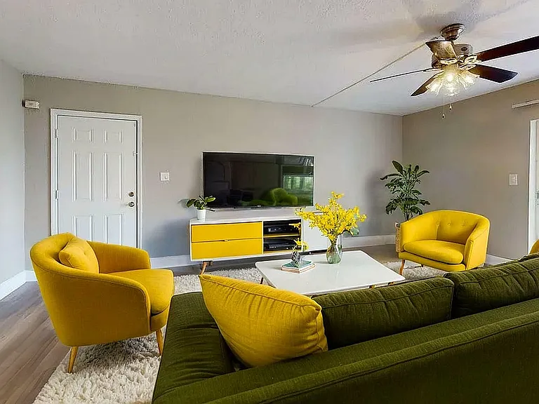 Vibrant living room with stylish yellow chairs, a comfy green sofa, and a sleek TV unit, enhanced by elegant decor and lush plants.