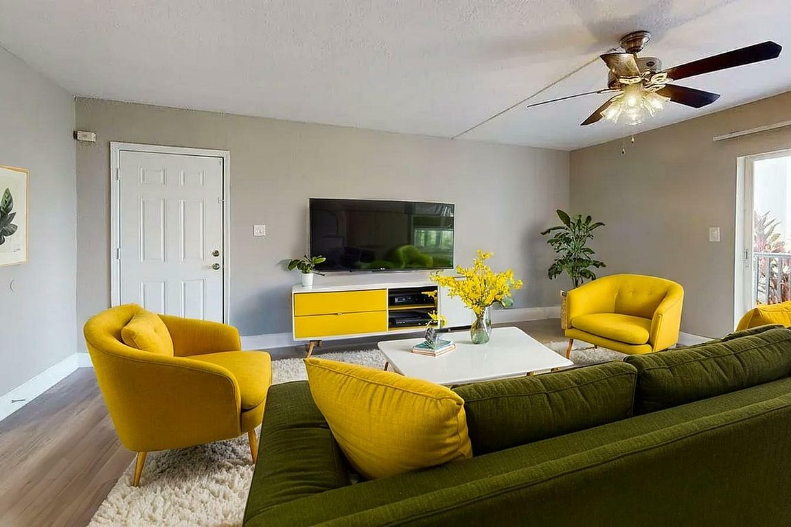 Vibrant living room with stylish yellow chairs, a comfy green sofa, and a sleek TV unit, enhanced by elegant decor and lush plants.