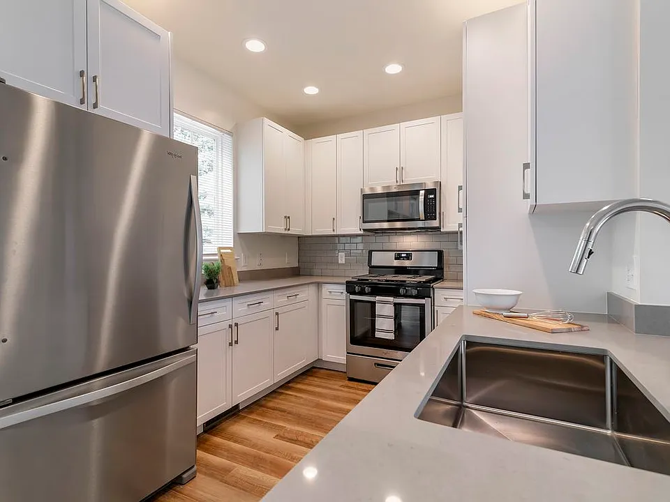 Renovated Package II kitchen with white cabinetry, grey quartz countertops, grey subway tile backsplash, stainless steel appliances, and hard surface flooring