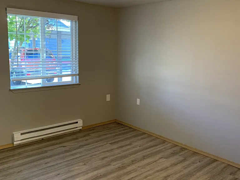 Bright and spacious master bedroom featuring wood-style flooring, neutral tones, and a sunlit window. Offers a clean, comfortable layout with plenty of room to relax and unwind.