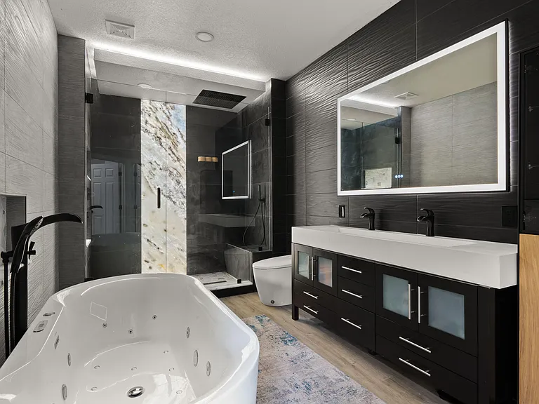 Spa-style bathroom featuring a soaking tub, glass-enclosed shower, and a double vanity with ample storage and a backlit mirro