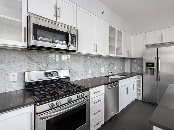 York House designer kitchen with gas stove, quartz countertops, stainless steel appliances, marble kitchen backsplash, and slate tile floor.