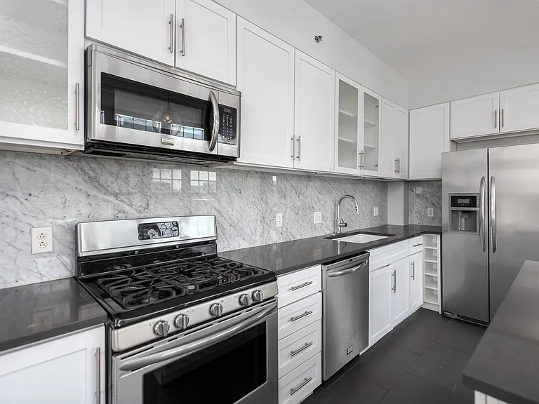 York House designer kitchen with gas stove, quartz countertops, stainless steel appliances, marble kitchen backsplash, and slate tile floor.