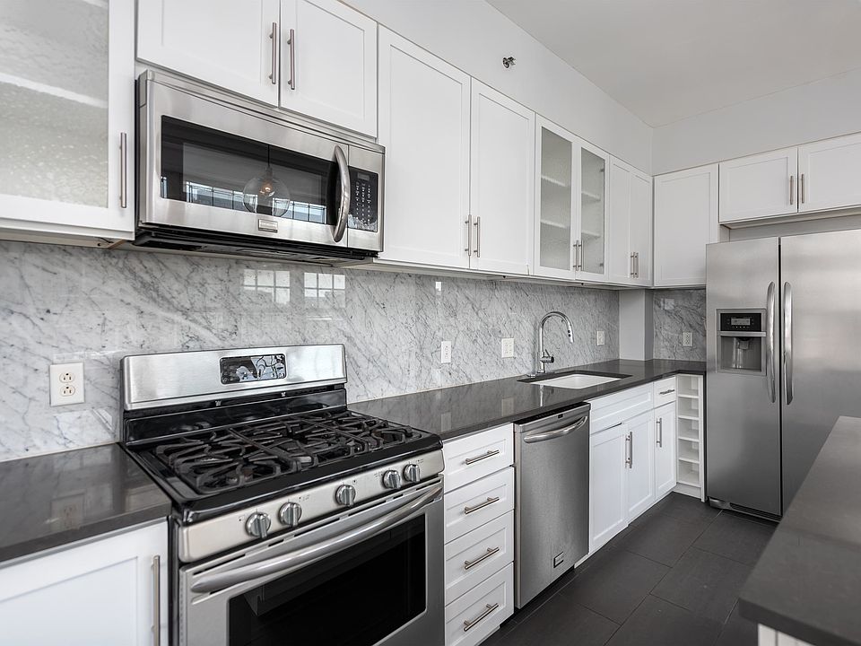 York House designer kitchen with gas stove, quartz countertops, stainless steel appliances, marble kitchen backsplash, and slate tile floor.