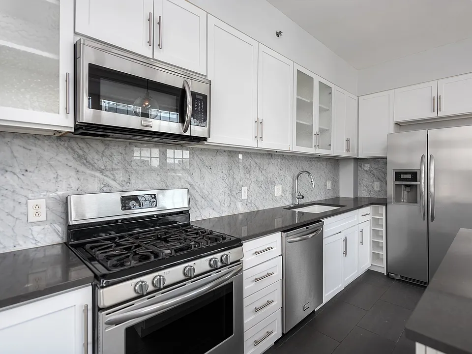 York House designer kitchen with gas stove, quartz countertops, stainless steel appliances, marble kitchen backsplash, and slate tile floor.