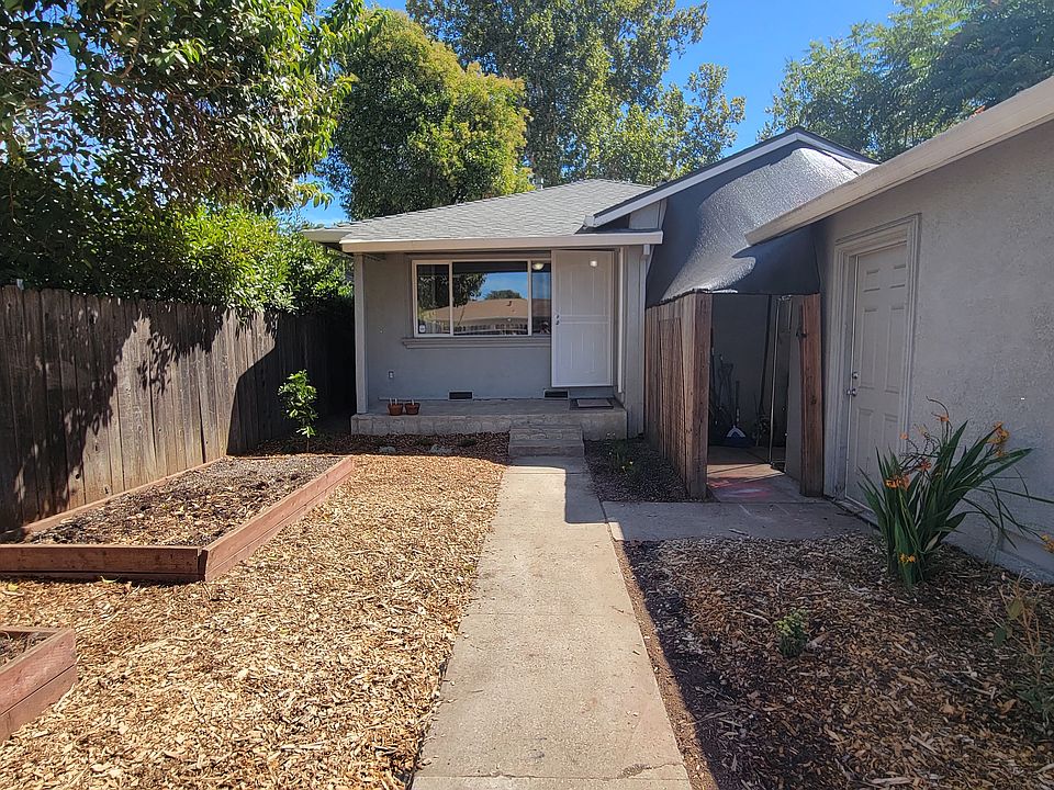 View of enclosed front yard, front door, 2 8'x4' raised beds, and detached garage on the right.