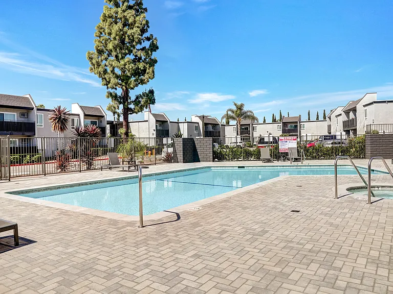 A swimming pool surrounded by a brick patio and a tall tree.
