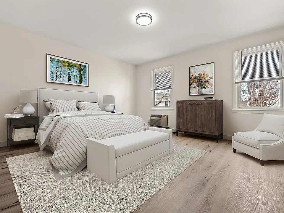 Bright and elegant bedroom featuring a cozy bed with striped linens, modern furnishings, and large windows with natural light.