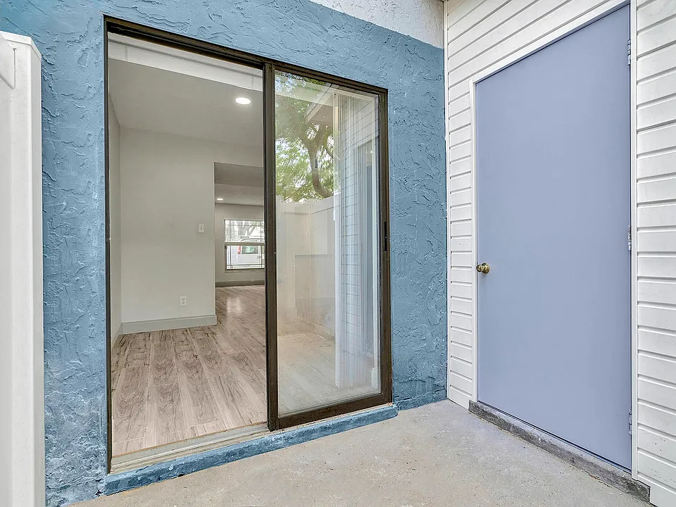 Inviting apartment entrance with modern sliding glass door opening to bright, spacious interior featuring elegant wood flooring.