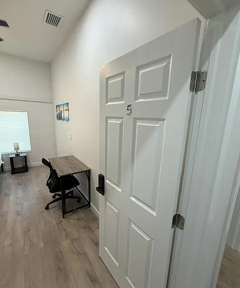 Private room with wood-style flooring, high ceilings, and a dedicated desk areaideal for work or study.