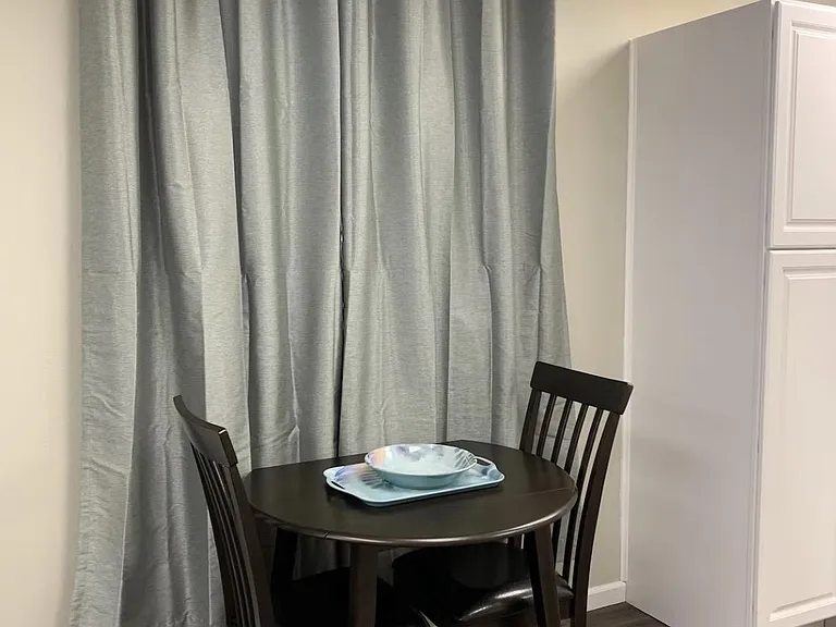 Compact dining nook with a two-seat table setup, easy-care flooring, and full-length curtains for added privacy.