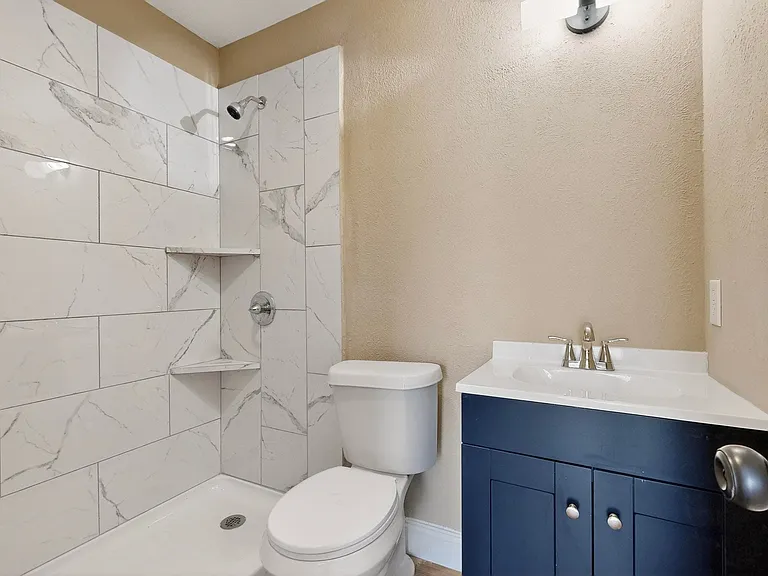 Bathroom featuring vanity, tiled shower, and a textured wall