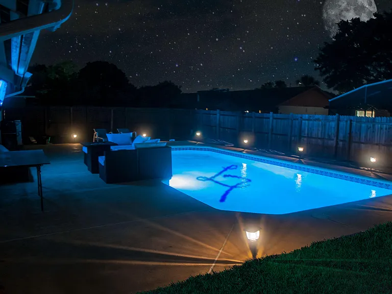 Fenced backyard retreat with an in-ground pool, patio seating area, and landscape lighting for evening enjoyment.