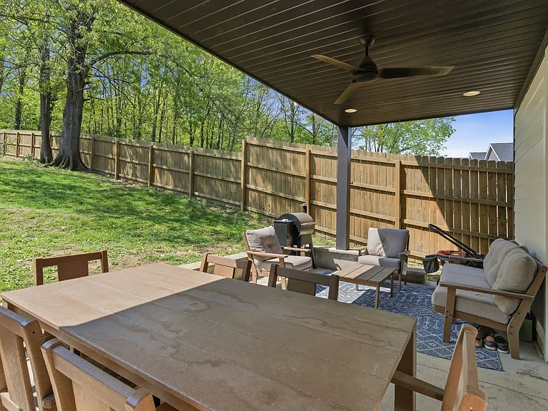 Backyard covered patio with tall privacy fence and view of open greenery.