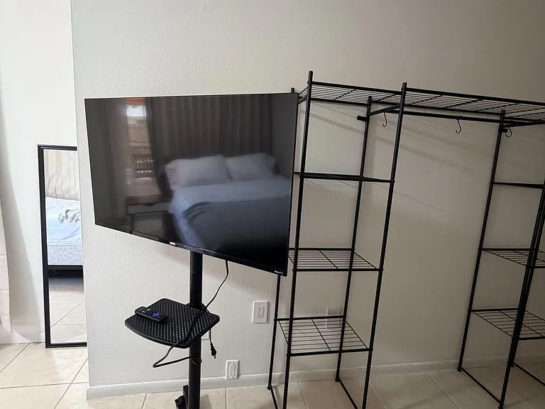 Versatile living area with tile flooring, a wall-mounted TV stand, and open metal shelving for easy storage.