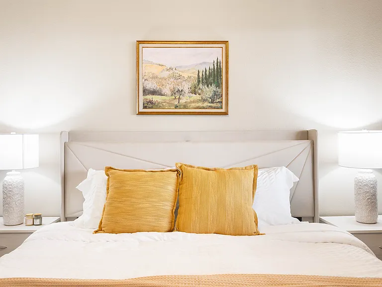 This vibrant bedroom features a white pure wall.A bed with wingback storage headboard,crisp white linens, and elegant nightstands with soft lighting create a restful sanctuary.