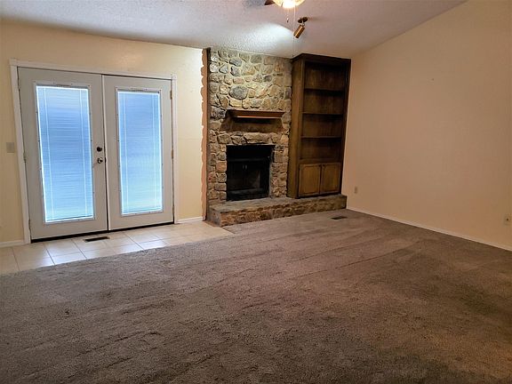 Living room, ceiling fan, fireplace, built-in bookshelf, patio doors lead to back open patio and fenced yard.