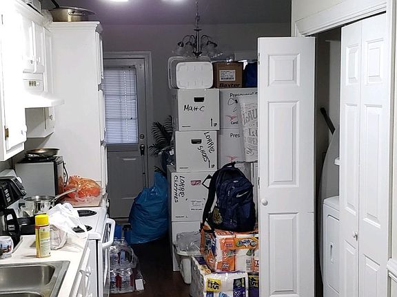 View through kitchen toward dining area (filled with moving boxes). Laundry closet on right. Notice vinyl plank flooring.