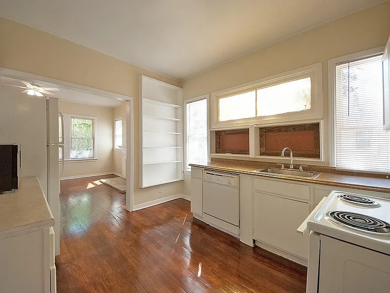 A cozy kitchen with white cabinets and shelves, a microwave, dishwasher and a stove, creating a clean and inviting cooking space.