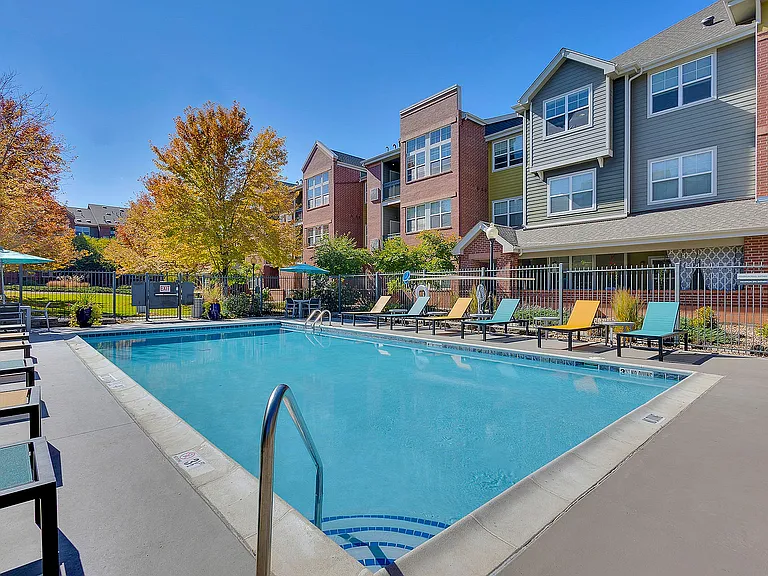Inviting residential complex with a sparkling pool, modern lounge chairs, and vibrant autumn foliage, perfect for relaxation and community living.