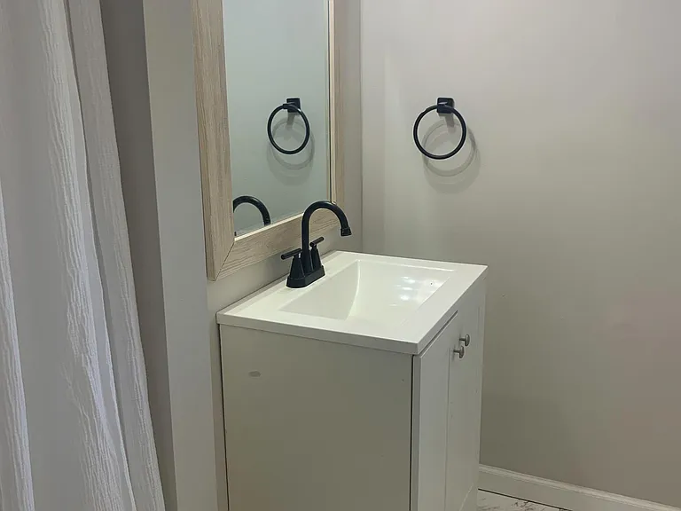 Bathroom vanity area with a single-sink cabinet, framed mirror, modern black fixtures, and tile flooring.