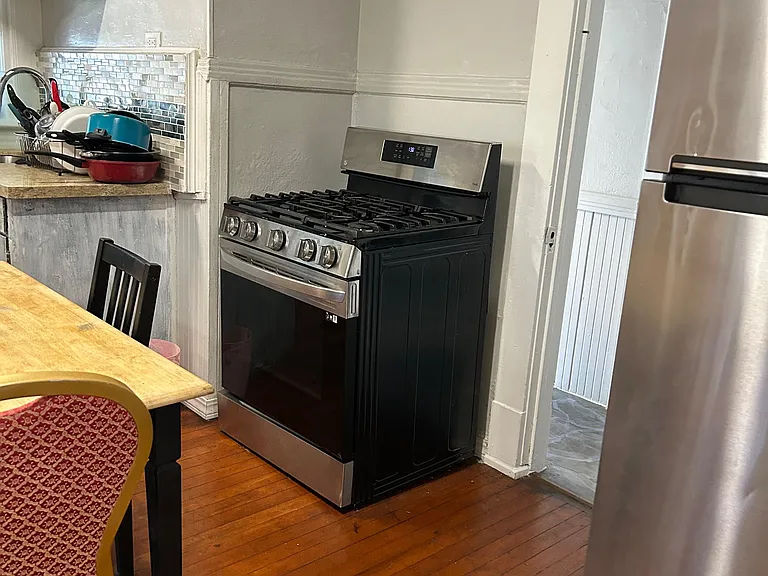 Kitchen features stainless steel gas range and refrigerator, with a tiled backsplash and adjacent eat-in table space.