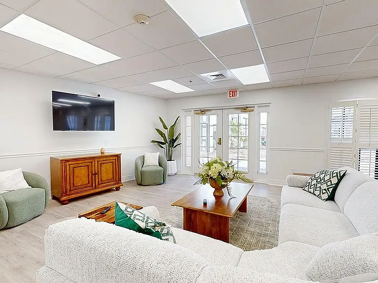 Inviting living room with plush white sectional sofa, elegant wooden furniture, and abundant natural light through large windows.