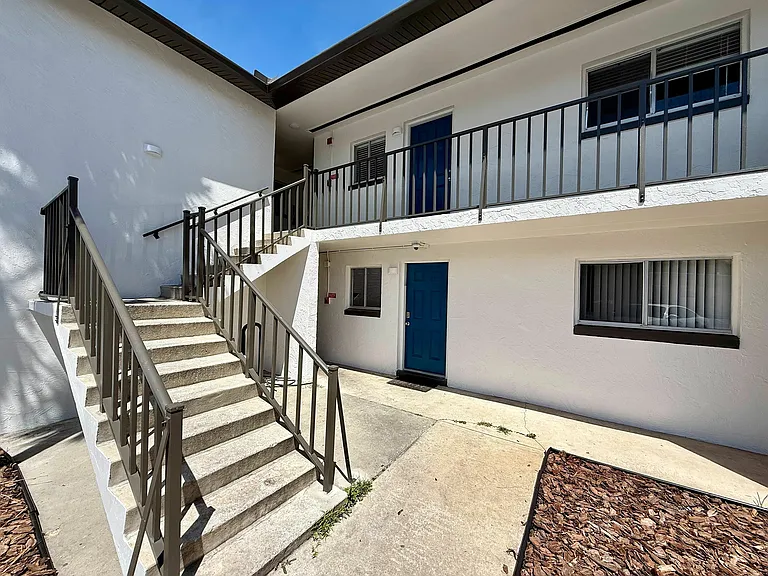 Inviting apartment exterior with a modern staircase leading to blue doors, emphasizing bright and welcoming entryways.