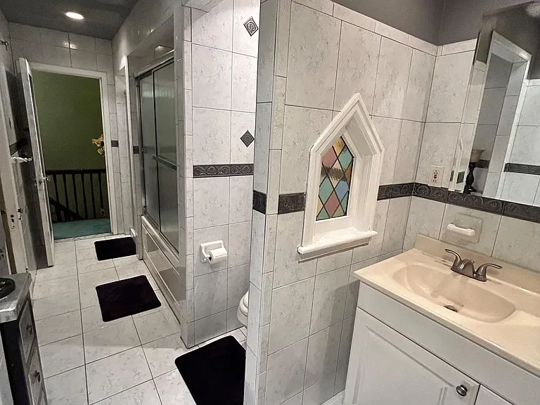 Tiled bathroom featuring a vanity with storage, wall mirror, and a tub/shower with sliding glass doors.