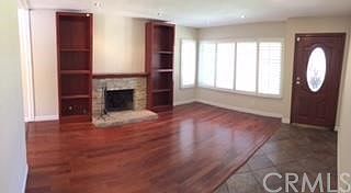 Living room with plantation shutters, newer windows, mahogany floors, quartz fireplace with custom built solid cherry mantle and shelves, scraped ceiling, 4 inch baseboards and mahogany front door.