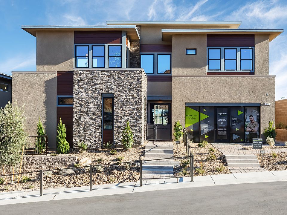 A modern, two-story residential building with a stone facade, large windows, and a landscaped front