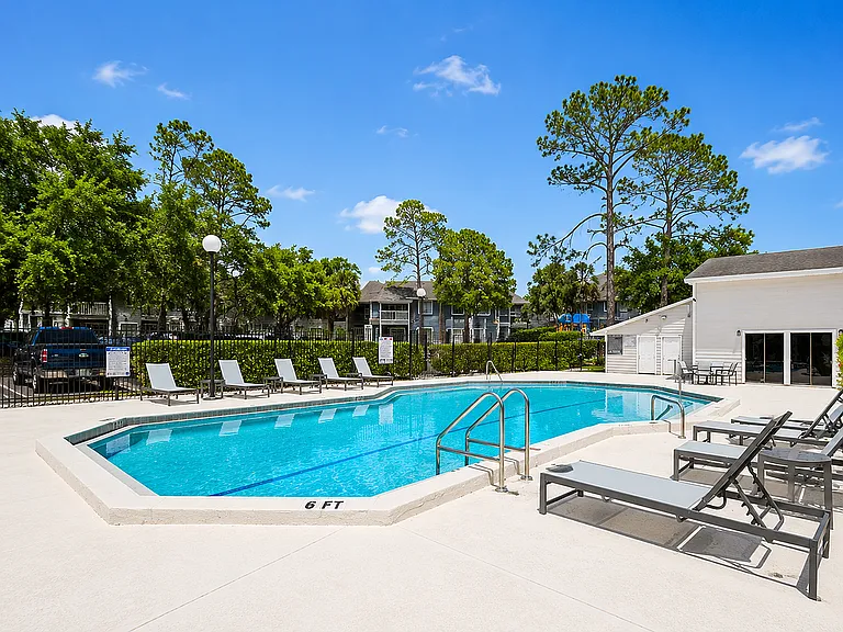 Inviting outdoor pool area with modern lounge chairs, surrounded by lush greenery and clear blue skies.